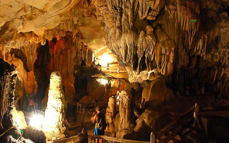 Intérieur de la grotte de Tham Chang à Vang Vieng, Laos, avec ses impressionnantes stalactites et stalagmites éclairées par des lumières artificielles et des visiteurs explorant les passerelles en bois