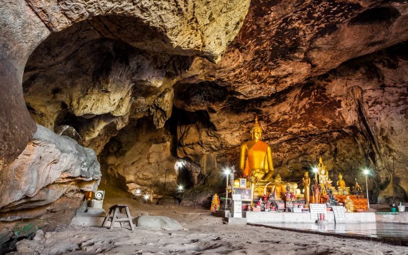 Statues de Bouddha dorées à l'intérieur d'une grotte sacrée à Wat Tham Suea, entourées de formations rocheuses naturelles éclairées