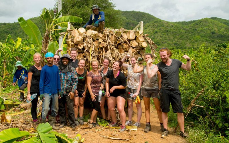 Groupe de volontaires engagés dans un projet communautaire en Asie, partageant un moment de solidarité et d’entraide au cœur d’un paysage rural verdoyant