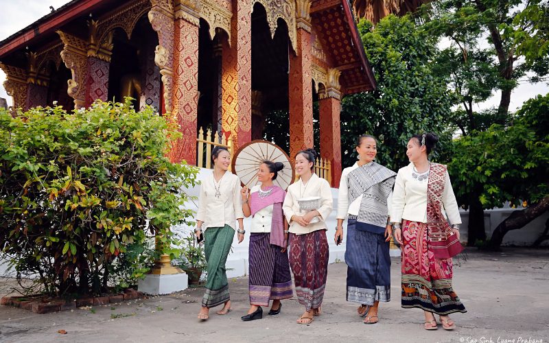 Femmes laotiennes en tenues traditionnelles marchant ensemble devant un temple richement décoré à Luang Prabang