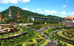 Vue panoramique du jardin tropical de Nong Nooch, avec ses aménagements paysagers impressionnants, ses statues et ses pavillons traditionnels sous un ciel bleu éclatant