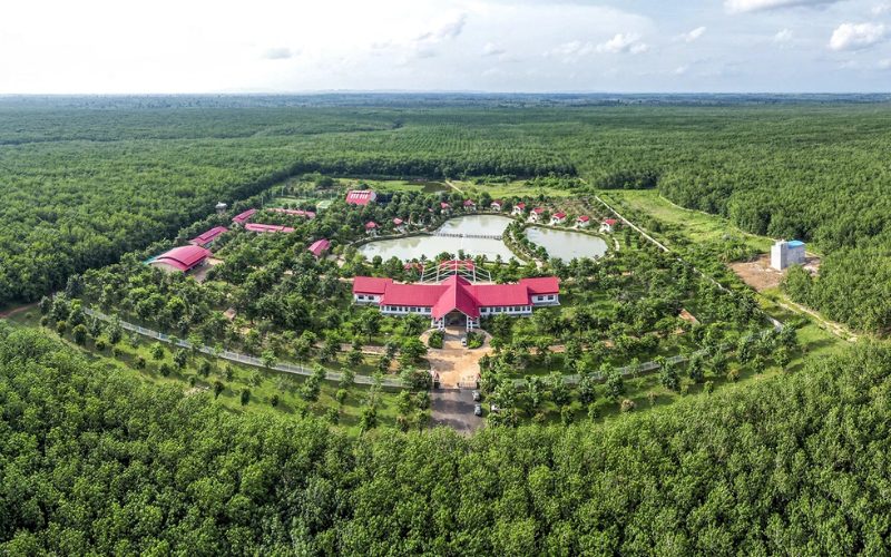 Vue aérienne d’un vaste domaine entouré de forêts, avec bâtiments aux toits rouges, jardins verdoyants et étangs aménagés dans un paysage rural paisible
