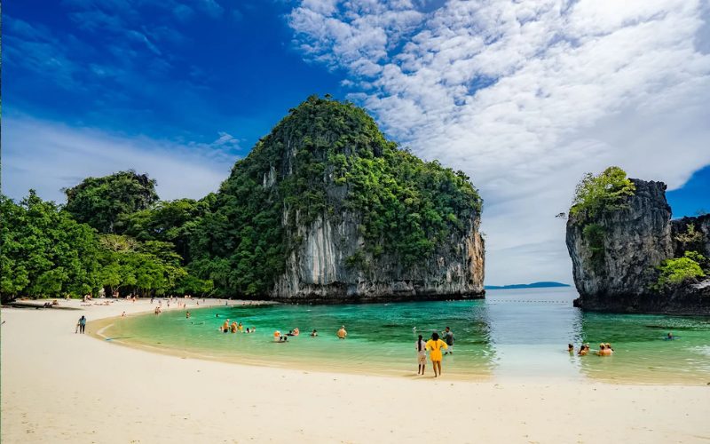 Plage de sable blanc à Koh Hong avec une eau turquoise cristalline, entourée de formations rocheuses imposantes couvertes de végétation luxuriante