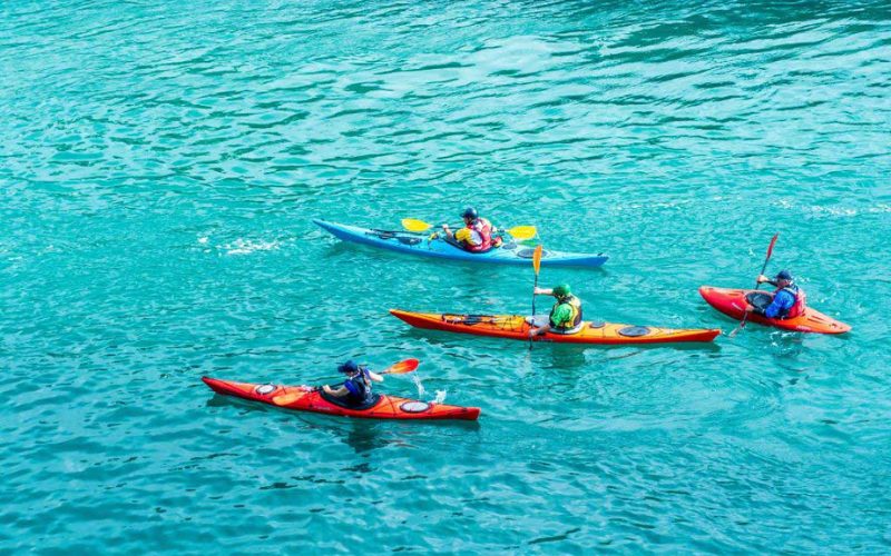 Quatre personnes pagayant en kayak coloré sur une eau turquoise limpide, profitant d’une activité nautique en plein air dans un cadre tropical.