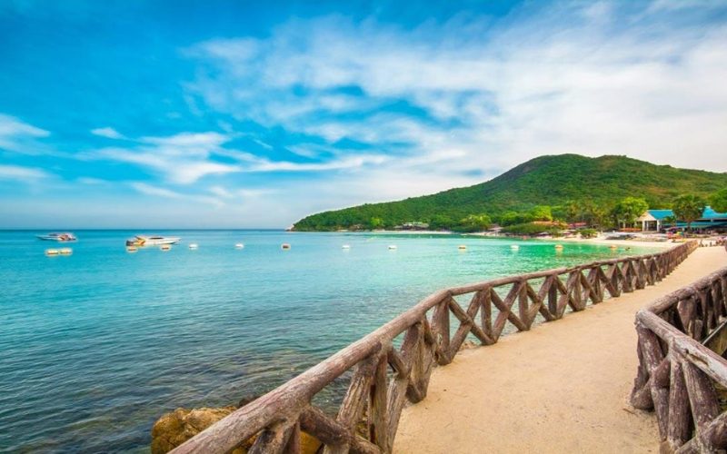Passerelle en bois menant vers la plage de sable blanc et la mer turquoise de l’île de Koh Larn, près de Pattaya, avec collines verdoyantes en arrière-plan