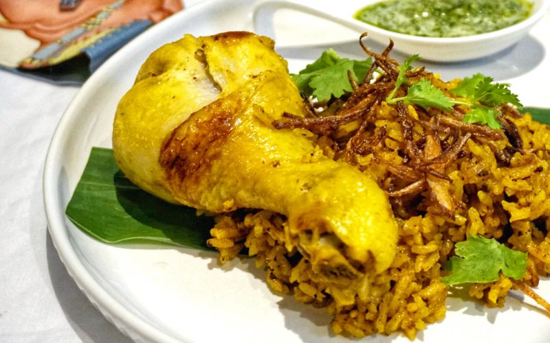 Assiette de Khao Mok Kai thaïlandais, composée de riz parfumé aux épices et d’un pilon de poulet rôti doré, garnie d’oignons frits et de coriandre