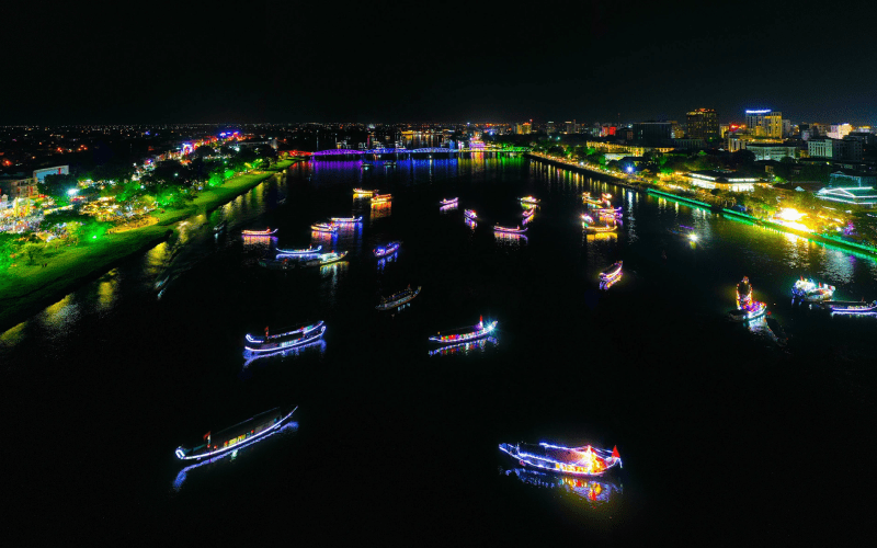 Vue nocturne spectaculaire de la rivière des Parfums à Hué, Vietnam, illuminée par des bateaux traditionnels décorés de lumières colorées et les reflets éclatants de la ville sur l’eau.