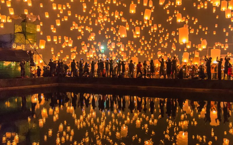 Des centaines de lanternes célestes s’envolant dans le ciel nocturne lors du festival des lanternes à Chiang Mai, reflétées dans l’eau
