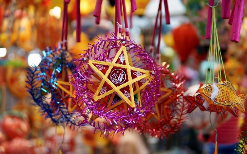Lanternes traditionnelles en forme d’étoile, ornées de guirlandes colorées, suspendues dans un marché animé à l’occasion du Tết Trung Thu au Vietnam