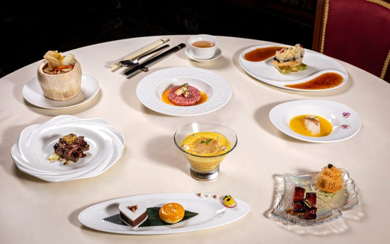 Table ronde élégamment dressée avec une sélection de plats gastronomiques raffinés, chacun présenté dans une assiette ou un bol individuel