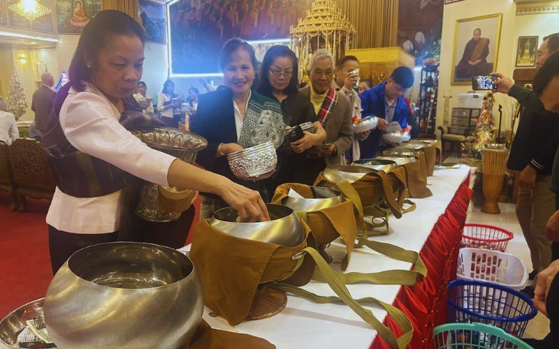 Moment de partage et de recueillement lors d’une cérémonie traditionnelle lao, où les fidèles déposent des offrandes dans le temple