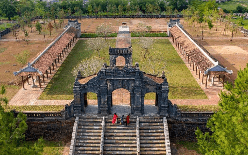 Vue aérienne du Temple de la Littérature (Văn Miếu) à Hué, Vietnam, mettant en valeur son architecture traditionnelle, ses toits en tuiles rouges, ses jardins symétriques et ses visiteurs en tenues traditionnelles. Les visiteurs pourront passer le voir durant une croisière sur la rivière des Parfums