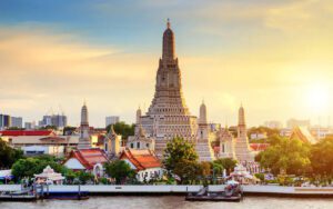 Vue panoramique du temple Wat Arun à Bangkok, Thaïlande, illuminé par les rayons dorés du lever du soleil, avec la rivière Chao Phraya au premier plan