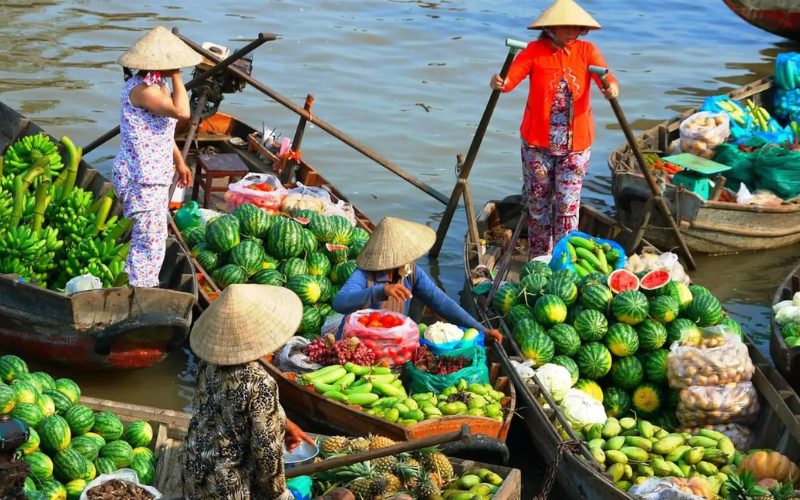 Bateaux chargés de pastèques, bananes et légumes au marché flottant du delta du Mékong, avec des commerçants vietnamiens en chapeau conique vendant leurs produits sur la rivière