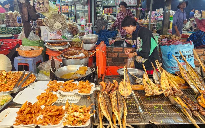 Stand animé au marché aux crabes de Kep, présentant une variété de fruits de mer frits et grillés, dont crevettes, poissons et calamars, préparés sur place dans une ambiance locale typique et chaleureuse