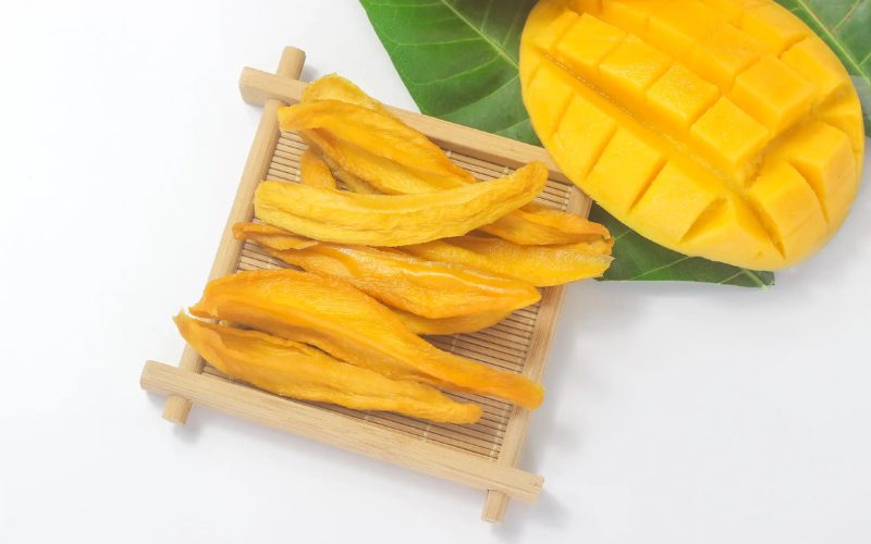 Tranches de mangue séchée disposées sur un plateau en bambou, accompagnées d'une mangue fraîche découpée en cubes sur une feuille verte