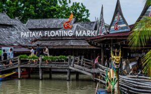 Entrée animée du marché flottant de Pattaya, avec passerelles en bois, maisons traditionnelles et visiteurs explorant les stands au bord de l’eau