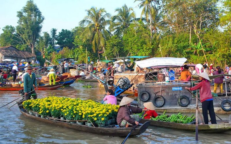 Marché flottant animé du delta du Mékong au Vietnam, où des commerçants en barques vendent des fleurs jaunes, des légumes et divers produits frais, entourés de nombreux bateaux traditionnels et de palmiers tropicaux en arrière-plan