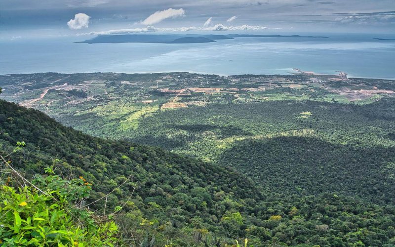 Vue panoramique depuis le sommet de la montagne de Bokor, avec une vaste forêt tropicale s'étendant jusqu'au littoral, et l'océan en arrière-plan sous un ciel partiellement nuageux