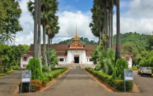 Entrée du Musée du Palais Royal à Luang Prabang, bordée de palmiers majestueux et de jardins verdoyants