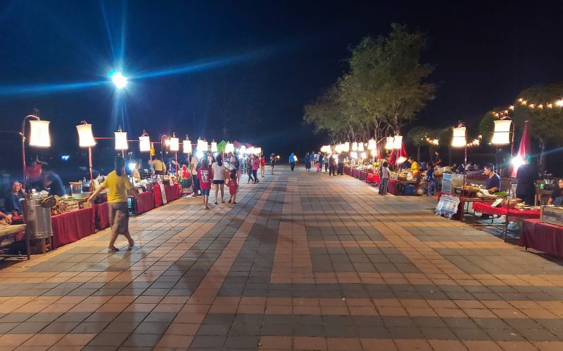 Marché nocturne de Sukhothai animé en soirée, avec stands de street food éclairés, vendeurs locaux et visiteurs flânant dans une ambiance conviviale