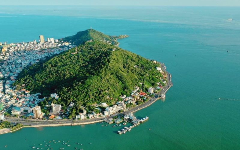 Vue aérienne de Vung Tau, au Vietnam, mettant en valeur la montagne verdoyante Nui Nho entourée de routes côtières, des bâtiments de la ville et des eaux turquoise de la mer