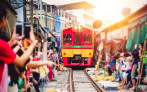 Train coloré traversant le célèbre marché ferroviaire de Mae Klong, au milieu des étals et des visiteurs prenant des photos