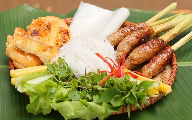 Plateau de nem lụi, brochettes de porc grillé sur tiges de citronnelle, servies avec vermicelles de riz, galettes de riz, légumes frais, herbes aromatiques, ananas, pain grillé et piments rouges