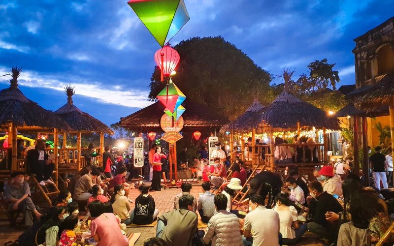 Soirée animée à Hoi An pendant la nuit du réveillon, avec des habitants et des visiteurs assis sous des pavillons en bambou décorés de lanternes colorées dans une ambiance festive et chaleureuse