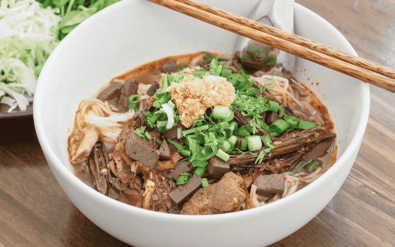 Bol de Nam Ngiao, une soupe de nouilles traditionnelle du nord de la Thaïlande garnie de viande, de cubes de sang, d’herbes fraîches et d’oignons hachés