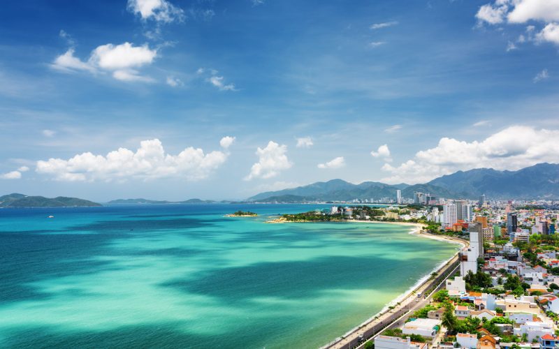 Vue panoramique de Nha Trang avec sa mer turquoise, son littoral urbain et les montagnes en arrière-plan sous un ciel bleu lumineux