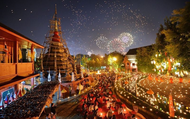 Célébration nocturne à Chiang Mai avec des lanternes illuminant un temple bouddhiste, des feux d’artifice dans le ciel et une foule réunie pour les festivités du Nouvel An lunaire