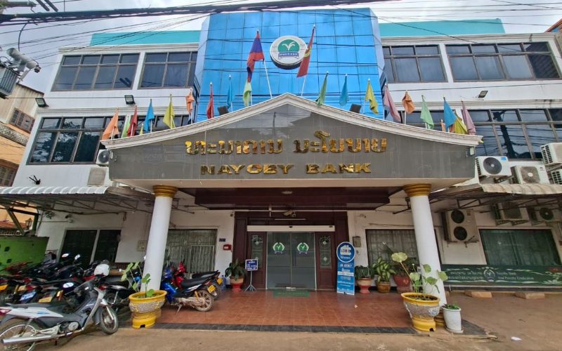 Façade d’une agence de la Nayoby Bank au Laos, avec l’entrée principale, le logo de la banque et des drapeaux nationaux