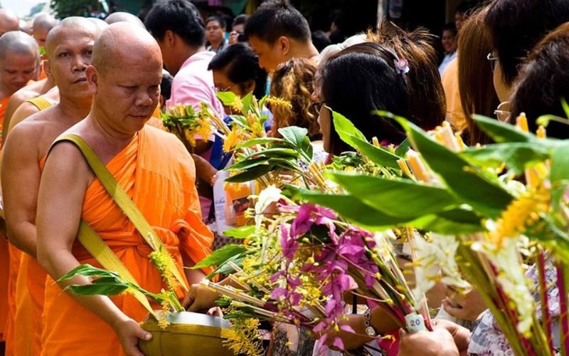 Des fidèles offrent des fleurs et des offrandes à une procession de moines bouddhistes en robe safran, lors d’une cérémonie traditionnelle de Khao Phansa
