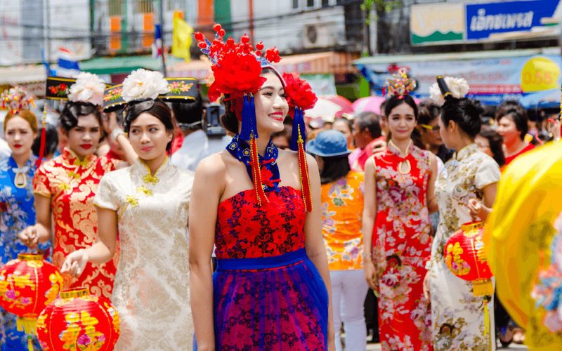 Jeunes femmes en costumes traditionnels chinois défilant dans les rues de Phuket lors du festival Por Tor, tenant des lanternes rouges décorées, sous un soleil éclatant et entourées d’une foule festive