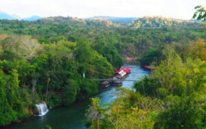 Vue panoramique d’une rivière entourée de forêt tropicale à Kanchanaburi, avec des maisons flottantes et une petite cascade au cœur de la nature verdoyante