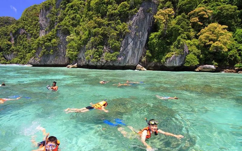 Touristes faisant du snorkeling dans les eaux turquoise entourées de falaises verdoyantes à Koh Phi Phi