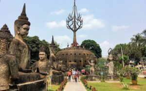 Promenade au milieu des impressionnantes sculptures bouddhistes et hindoues du parc de Bouddha avec des visiteurs explorant le site et montant sur la structure centrale ornée d’un arbre symbolique