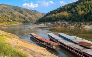 Bateaux traditionnels amarrés sur les rives du Mékong, entourés de collines verdoyantes et d’un paysage naturel paisible au Laos