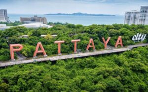 Vue aérienne du célèbre panneau “Pattaya City” entouré de verdure luxuriante, avec la mer et les immeubles en arrière-plan