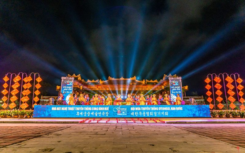 Spectacle nocturne du Festival de Huê devant la Cité impériale, avec des artistes en costumes traditionnels, une scène illuminée, des lanternes colorées et des jeux de lumière sous le ciel de nuit