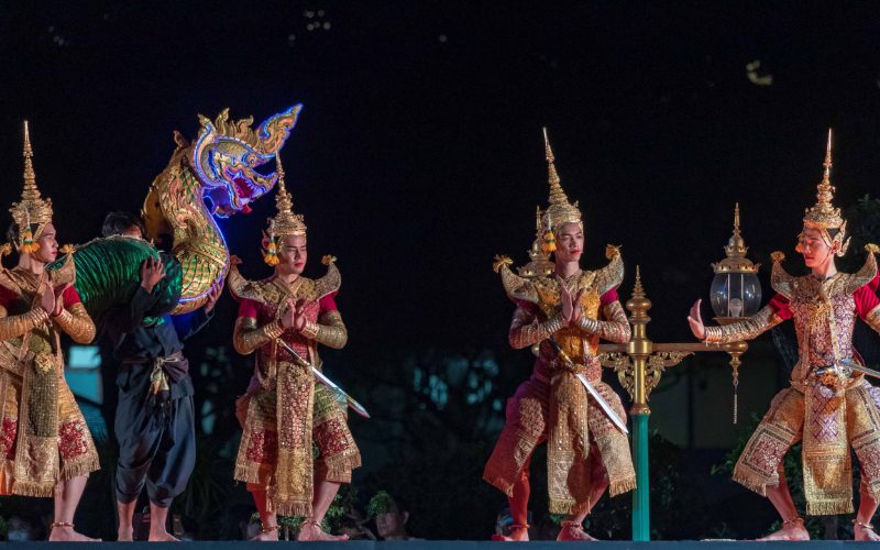 Danseurs thaïlandais en costumes traditionnels richement ornés effectuant une performance culturelle nocturne, avec une figure de naga illuminée en arrière-plan