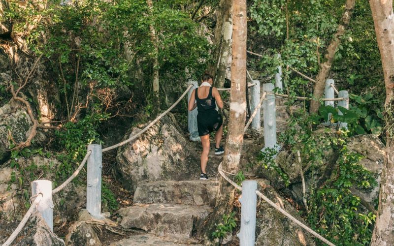 Randonnée sur un sentier forestier du parc national marin d’Ang Thong, avec une visiteuse gravissant des marches en pierre entourées de végétation tropicale dense