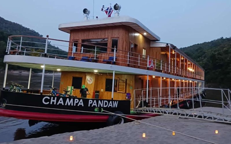 Le bateau de croisière RV Champa Pandaw amarré sur le Mékong au Laos, avec ses ponts en bois éclairés au crépuscule et les collines verdoyantes en arrière-plan