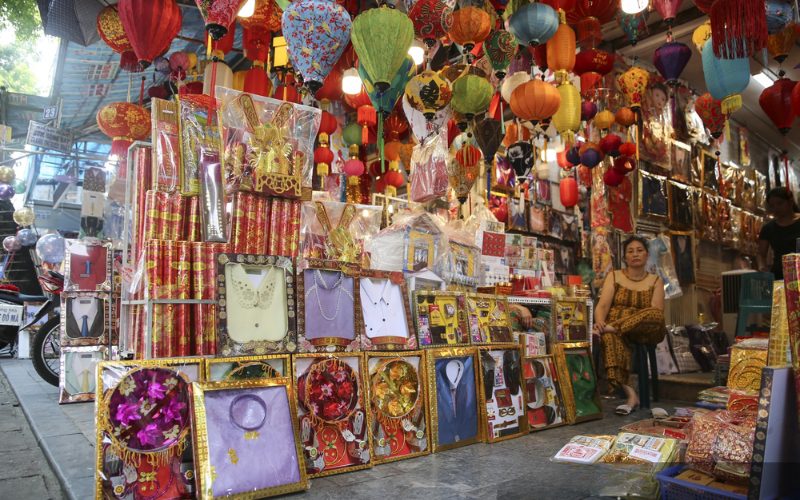 Un étal coloré dans une rue vietnamienne vendant des objets votifs en papier – vêtements, bijoux, lingots d’or, et lanternes – destinés à être brûlés pour honorer les ancêtres lors de la fête du Vu Lan