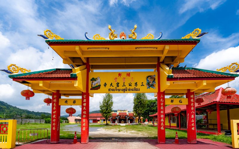 Portail jaune et rouge richement décoré du sanctuaire chinois San Chao Mae Yanang à Phuket, orné de lanternes rouges, de sculptures de dragons dorés et d’inscriptions chinoises
