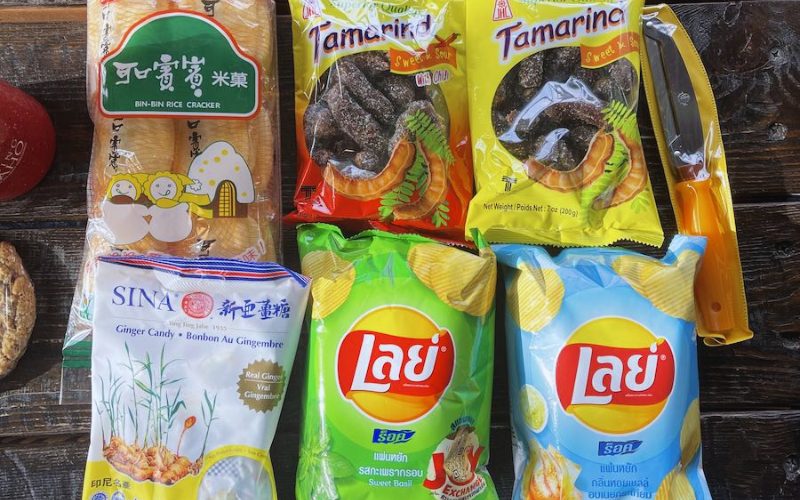 Assortiment de snacks thaïlandais comprenant des chips Lay’s aux saveurs locales (basilic doux et ail), des bonbons au gingembre, des crackers de riz Bin-Bin et des bonbons au tamarin emballés dans des sachets colorés