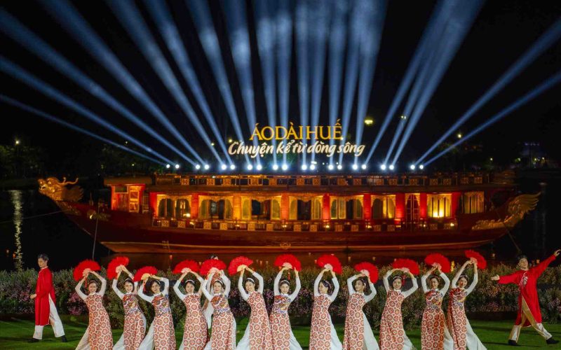 Spectacle nocturne du Festival de Huê sur la rivière des Parfums, avec danseuses en áo dài traditionnels, éventails rouges et jeux de lumières illuminant une scène flottante