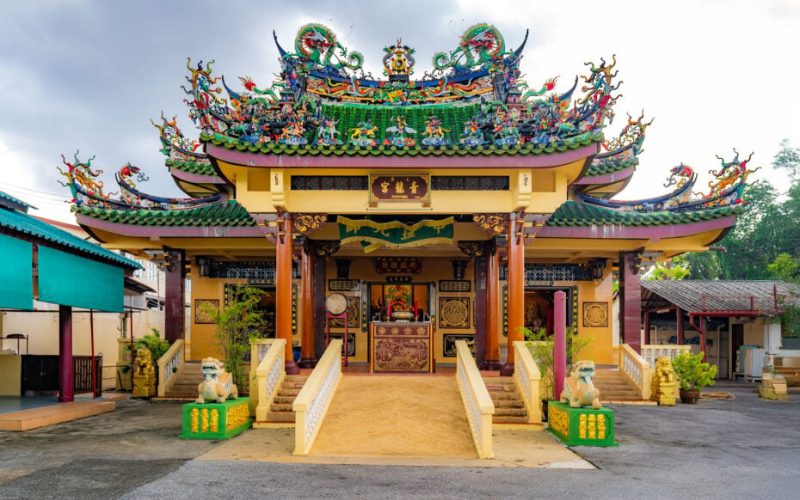 Façade richement décorée du sanctuaire chinois San Chao Jeng Ong à Phuket, avec un toit vert orné de sculptures colorées de dragons et de figures mythologiques