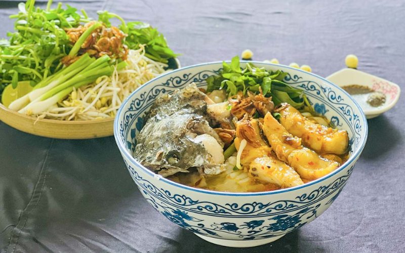 Bol de bánh canh cá lóc, soupe vietnamienne aux nouilles épaisses et poisson-tête-de-serpent, servi avec herbes fraîches et pousses de soja